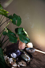 scene showing a table with gemstones in a wooden box , incense stick smoking and a monstera plant...