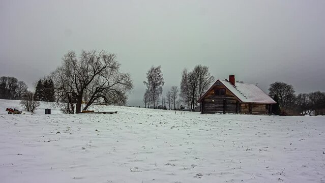 Timelapse shot of dark cloud movement over a wooden cottage surrounded by thick layer of white snow on a winter day.