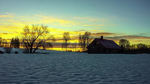 Timelapse shot of sun setting through clouds behind beautiful wooden cottage surrounded by thick layer of white snow on a winter evening.