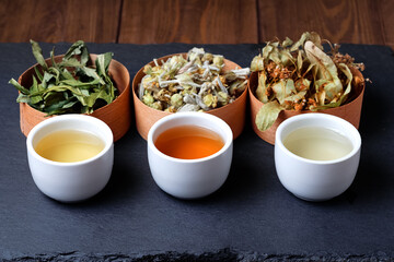 Herbal tea in small cup with dry tea on black background. Side view.
