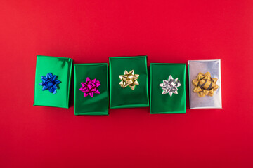 Creative handmade christmas green and silver paper gift boxes with decor on red background, top view.