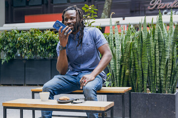 african man sitting outdoors sending voice message on his phone.