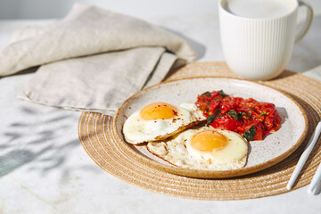 Breakfast with fried eggs and fried tomatoes with spinach on plate and cup of latte coffee