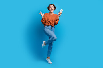 Full size photo of attractive young woman raise hand impressed hold gadget dressed stylish brown clothes isolated on blue color background