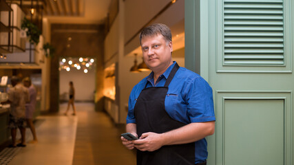 Fototapeta premium Businessman owner of a cafe stands at the entrance with a phone in his hand.