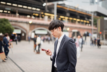 新橋の駅前でスマートフォンを見るビジネスマン