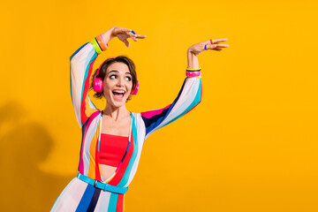 Fototapeta na wymiar Photo of excited shiny lady wear striped costume enjoying pop songs headphones looking empty space isolated yellow color background