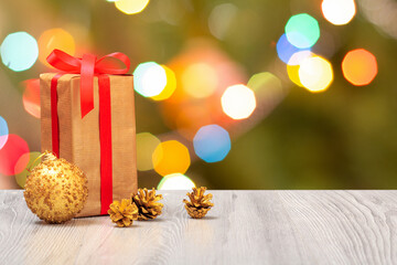 Gift box, cones and a toy ball on wooden boards with blurred twinkling party lights