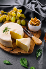 Round cheese on a wooden board and green grapes