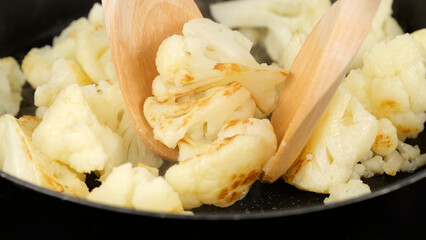 Fried cauliflower stirring with spoon in pan
