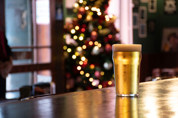 pint of lager beer pilsner right corner on a pub counter decorated for Christmas with a blurred...