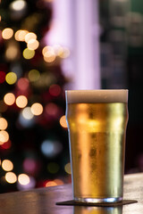 pint of lager pilsner beer on a pub counter decorated for Christmas with a blurred tree in the background and blinking lights