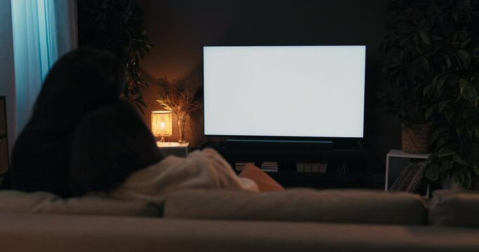 Relieved young women sitting in the living room on couch at home watching tv white screen mockup concept.