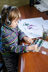 Blond toddler baby boy listening to music and drawing at home. Child has activity time with watercolor paint