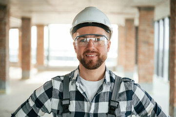 Positive smiling construction worker in uniform in empty unfinished room