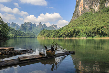 Landscape of karsten mountain along the Li River in Guilin with a bamboo raft and two comorants perching on fish basket - obrazy, fototapety, plakaty