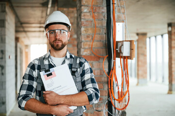 Electrician with notebook. Construction worker in uniform in empty unfinished room