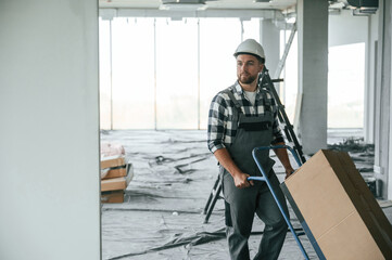 With large box, transporting the material. Construction worker in uniform in empty unfinished room