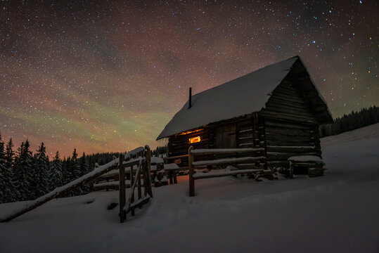 Wooden log cabin in winter mountains under starry sky