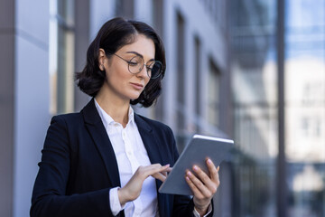 A young female lawyer is standing outside the courthouse in a business suit and glasses and is...