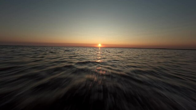 fpv drone flies low over the water of a large lake against the background of the setting sun fast flight over the water waves reflect the sunset evening. High quality 4k footage nobody towards the sun