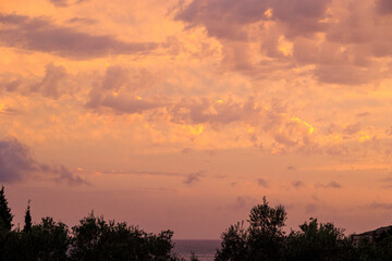Colourful sunset in the bay of Agios Georgios with dark clouds in front of an intensely orange sky with individual strangely shaped dark wispy clouds on the island of Corfu