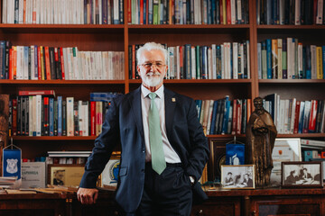 Experienced mature rector confidently posing in university library surrounded by books. Successful...