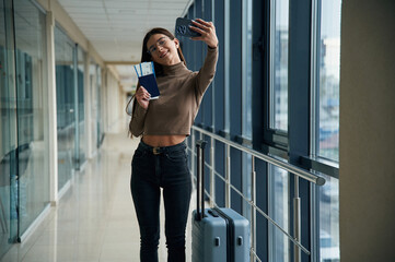 Making selfie with phone, smiling. Young woman traveler in the airport entrance hall