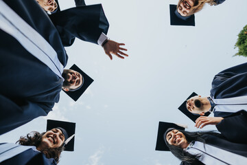Graduates in gowns and caps celebrate achievement, putting hands together in joy. Inspiring outdoor...