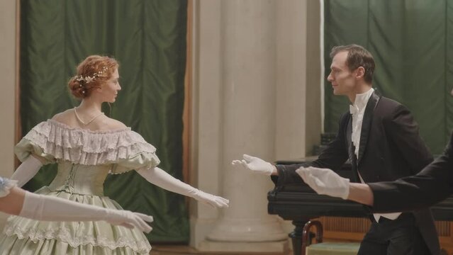 Medium slowmo shot of two Caucasian aristocratic men stretching their hands while inviting women to dance with them during ceremonial reception with ball
