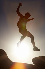Man, silhouette and jump on rock at sunset with freedom, adventure and challenge on mountain or...