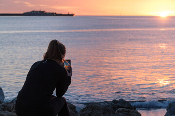 Paseo marítimo Málaga, amanecer, mujer mirando el móvil, haciendo fotos de los primeros rayos de...