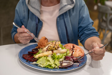 Mature Caucasian woman enjoying a mixed salad of fresh vegetables, beets, asparagus, cheese and...