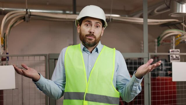 Metallurgical plant worker stands in a technical room, spreading his arms. Man gestures uncertainty, indicating unresolved technical malfunction, a problem in the electrical network system failure.