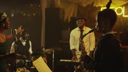 Medium shot of African American jazz quartet making performance on stage in fancy jazz club in evening