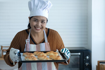 Happy homemade bakery chef, woman wearing a chef's hat and apron proudly presents bread fresh from the oven, small business