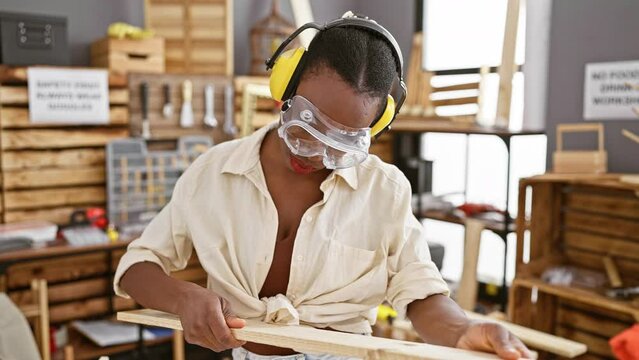 Attractive african american woman carpenter, smiling with confidence as she holds a wood plank in a carpentry workshop