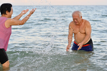 Senior happy couple having playful fun in the sea, splashing water at each other, Active elderly travel concept