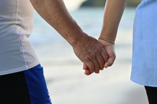 Close-up image of an elderly couple holding hands while walking around the seashore