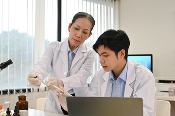 Two professional Asian scientists concentrated on doing a chemical experiment in the lab