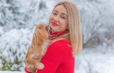 Smiling happy Lady with a young Pekingese cute dog in the snow park playing outdoor .Winter Christmas time. Doggo in good mood on a walk with his owner