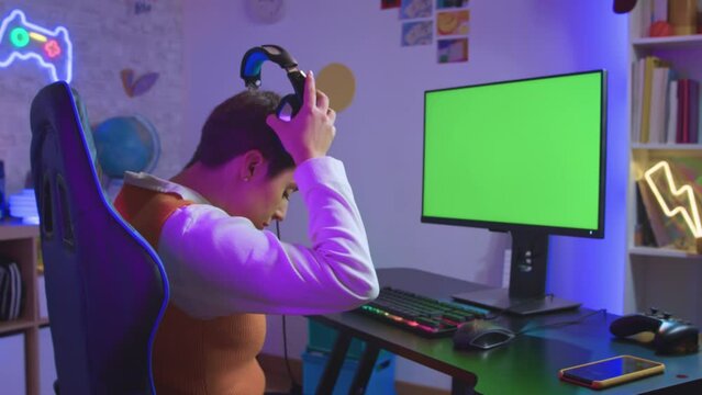 girl with short hair puts on her headphones to play a video game on her computer. Green screen for adaptations. High quality 4k footage