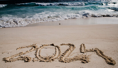 2024 written in white sand on tropical beach, happy New Year