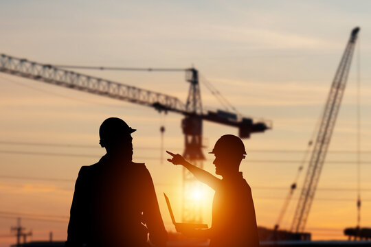 Silhouette of Engineer and foreman worker checking project at building site, construction site blurred sunset in evening time background