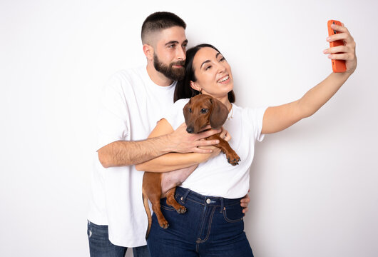 Young couple with her dachshund dog taking a selfie standing isolated over white background.