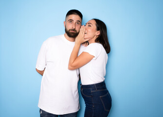 Naklejka premium Brunette whispering secret to her boyfriend on blue background