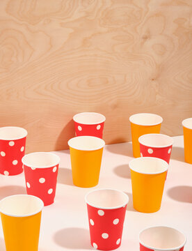 A pattern of paper cups for various drinks in bright yellow and red with white polka dots on a wooden background. Birthday celebration.