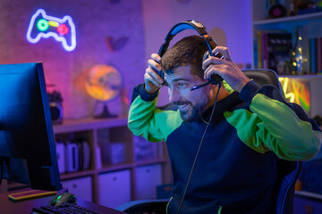 Gamer playing excited online video game with headphones streaming on computer in a neon light room....