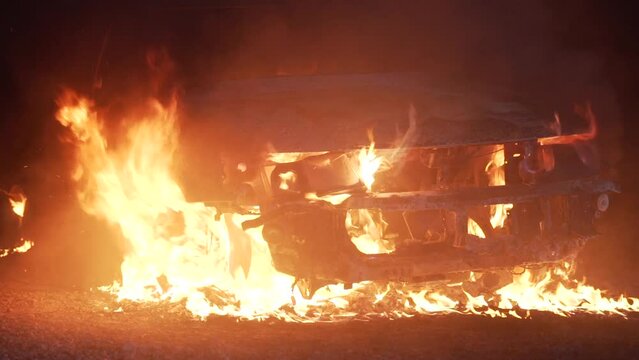Cinematic film shot of a vehicle burning in flames after a car crash at night. Vehicle accident concept. High quality 4k footage in slow motion with copy space for text.