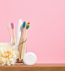 Organic wood toothbrushes with colorful bristles in glass. Dental floss on a pink background. Copy...